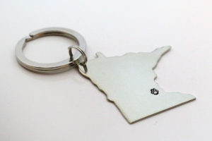 Silver Minnesota-shaped keychain with pay print marketing the Twin Cities location